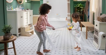 Two young children playing with toilet paper in the bathroom.