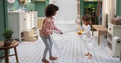 Two young children playing with toilet paper in the bathroom.